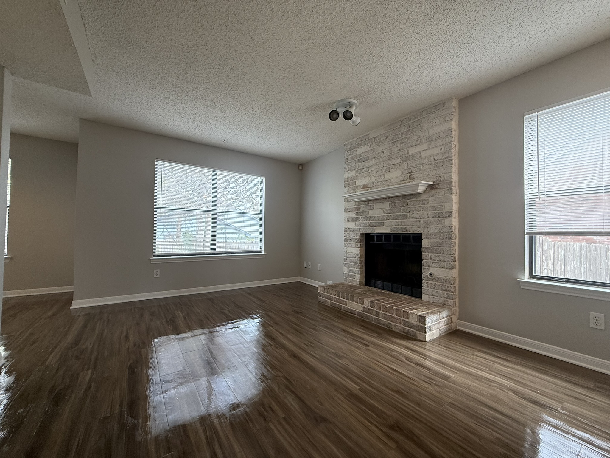 7806 Topawa Cove, Unit A Austin, TX 78729 - Photo 7 of 25 Unfurnished living room featuring a brick fireplace, a textured ceiling, and dark wood-style flooring