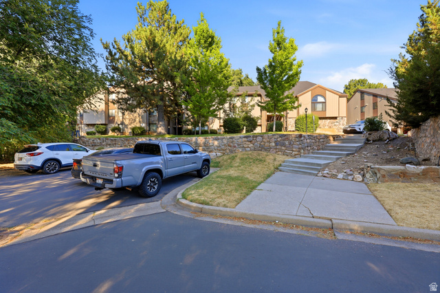 1175 Canyon Road, Unit 86 Ogden, UT 84404 - Photo 4 of 29 Property exterior featuring tan siding, a stone retaining wall, mature trees, and concrete steps