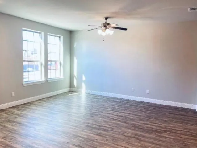 an empty room with wooden floor chandelier fan and windows