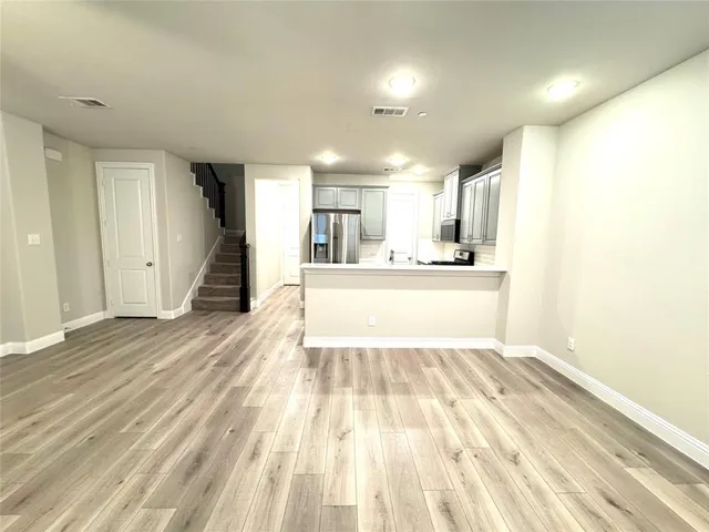 a view of an empty room with wooden floor and a kitchen