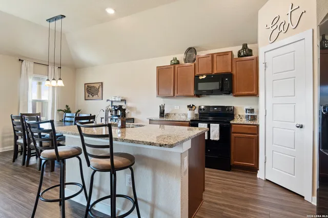 a kitchen with stainless steel appliances granite countertop a stove top oven a sink a dining table and chairs with wooden floor