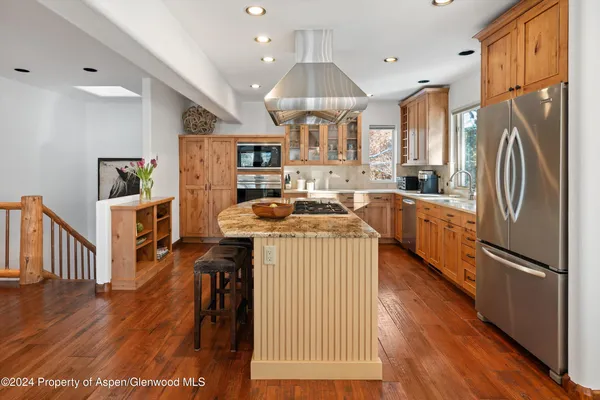 a kitchen with stainless steel appliances granite countertop a refrigerator a sink dishwasher a stove and white countertops with wooden floor