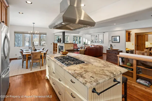 a kitchen with stainless steel appliances granite countertop a stove top oven a dining table and chairs with wooden floor