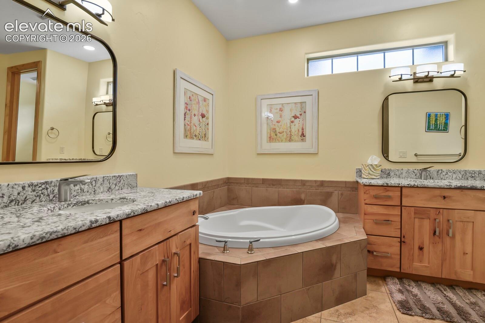 5545 Wilson Road Colorado Springs, CO 80919 - Photo 20 of 48 Dual wood-finish vanities with stone countertops, a built-in soaking tub with tile surround, and an upper transom window