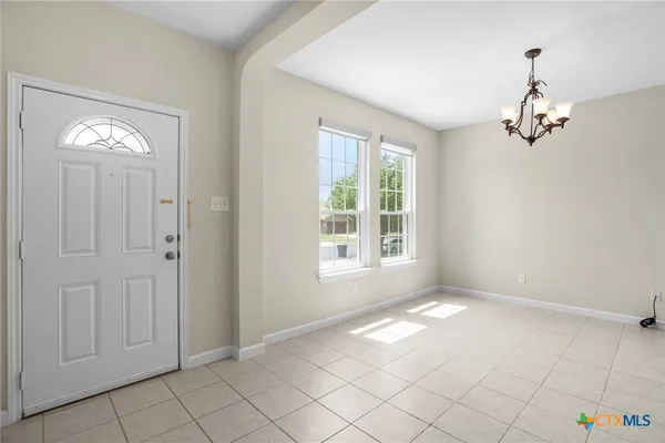 a view of an empty room with window and chandelier fan
