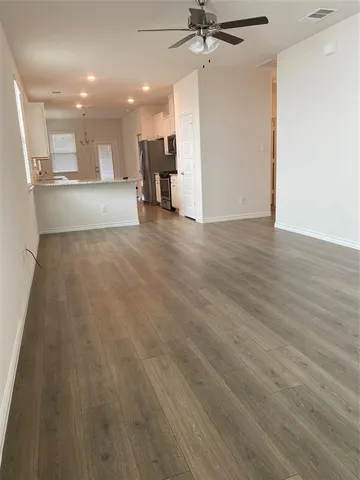 an empty room with wooden floor a ceiling fan and kitchen view