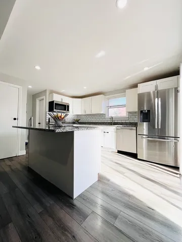 a kitchen with stainless steel appliances granite countertop a refrigerator a stove a sink and white cabinets with wooden floor