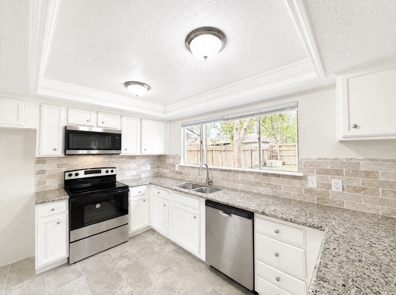 8407 Riverside Walk Lane Houston, TX 77064 - Photo 6 of 33 Renovated kitchen featuring white cabinetry, granite countertops, new stainless steel appliances, and a large window overlooking the lush, huge backyard.