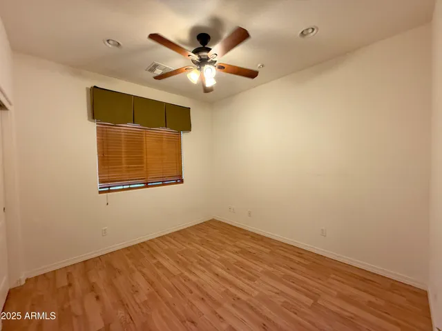a view of an empty room with wooden floor and a ceiling fan