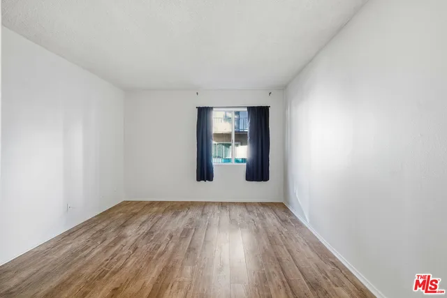 a view of an empty room with wooden floor and window