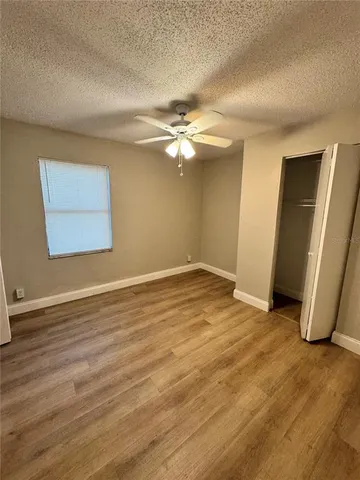 an empty room with wooden floor chandelier fan and windows