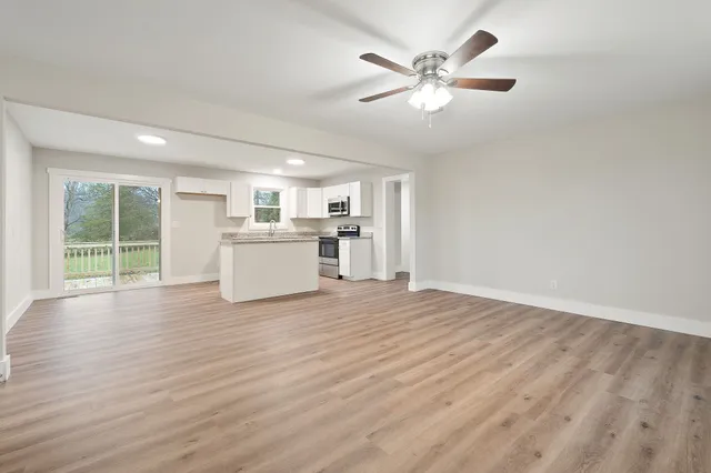 a view of a livingroom with a kitchen stove wooden floor and a ceiling fan