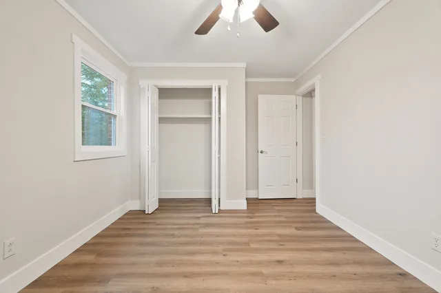 an empty room with wooden floor chandelier fan and windows