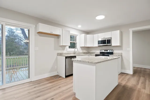 a kitchen with stainless steel appliances granite countertop a stove a sink a refrigerator white cabinets and wooden floor