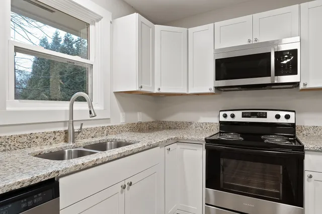 a kitchen with stainless steel appliances granite countertop white cabinets and a stove top oven