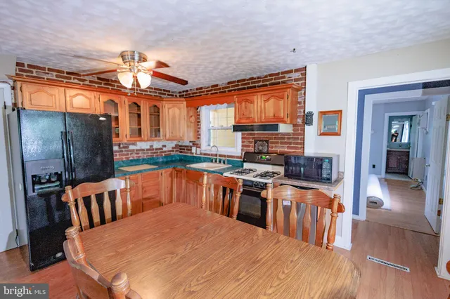 a kitchen with stainless steel appliances kitchen island granite countertop a refrigerator a stove top oven and a dining table with wooden floor
