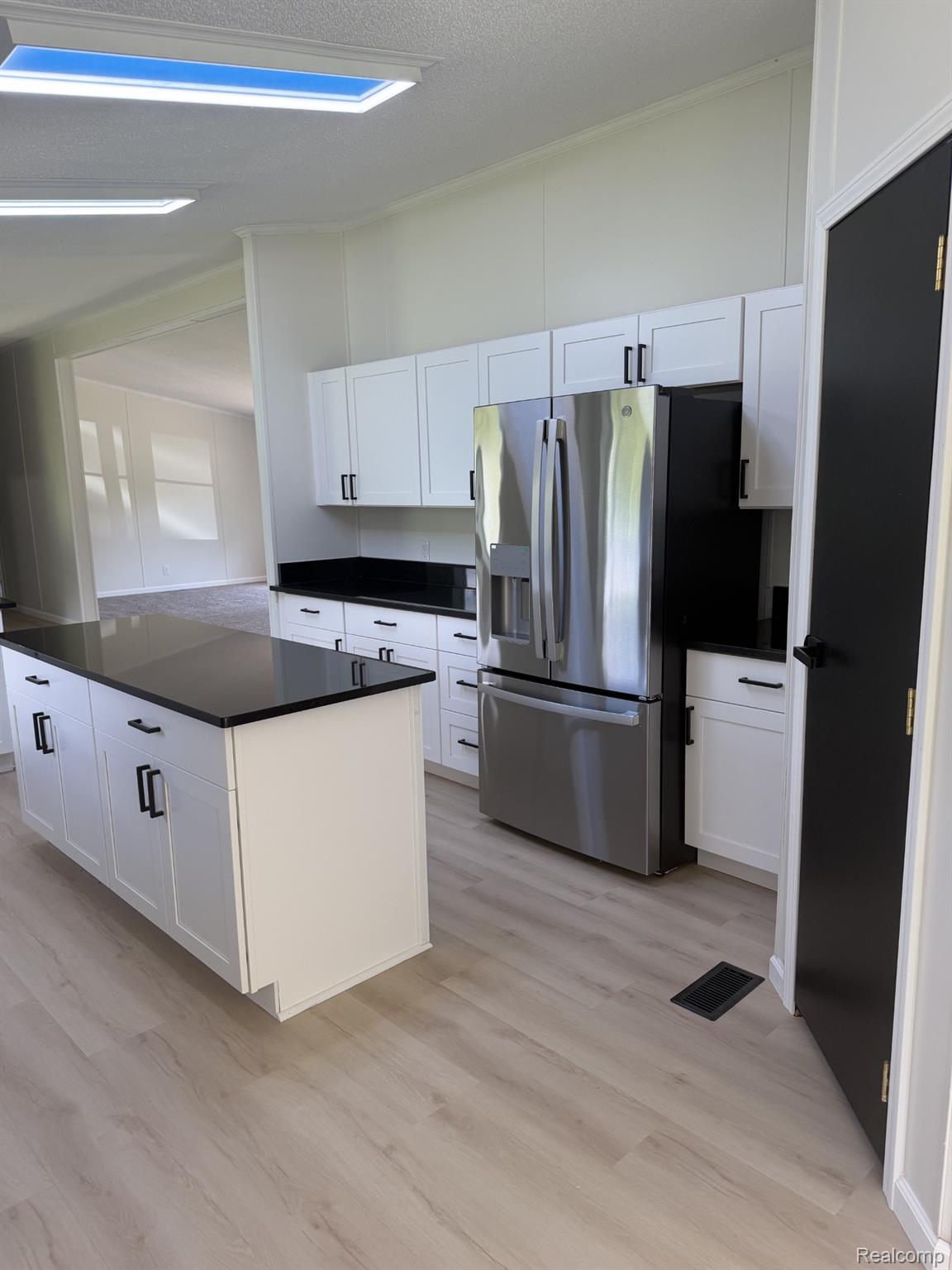 3586 Columbiaville Road Columbiaville, MI 48421 - Photo 4 of 10 Modern kitchen featuring an island, white cabinetry with dark hardware, dark countertops, a stainless steel refrigerator, and wood-finish flooring