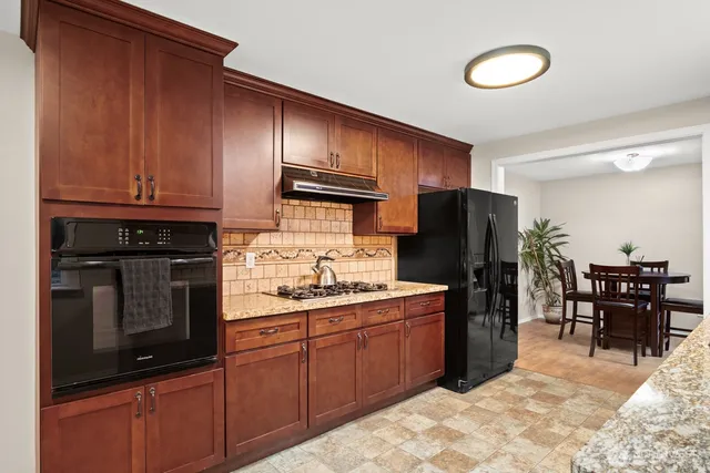 a kitchen with stainless steel appliances granite countertop a refrigerator stove top oven dining table and chairs