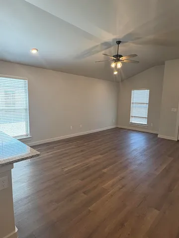 an empty room with wooden floor chandelier fan and windows
