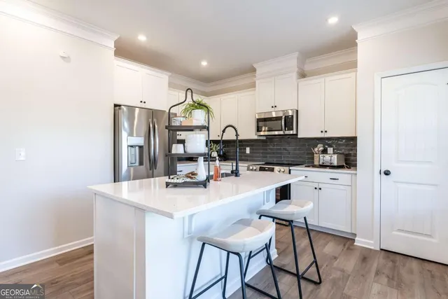 a kitchen with stainless steel appliances granite countertop a stove a sink a refrigerator a microwave oven with white cabinets and wooden floor