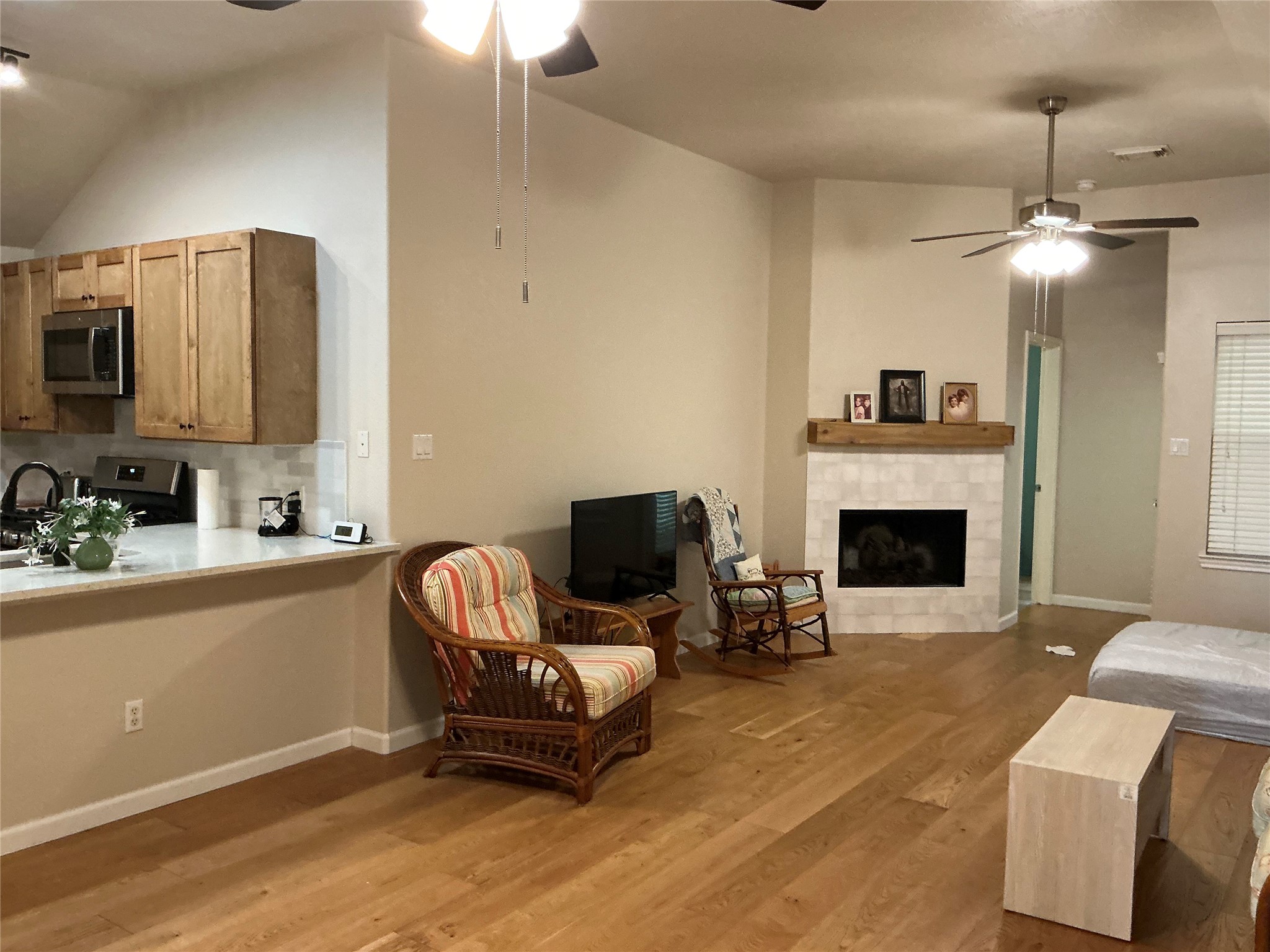 2910 Crescent Bend Road Spring, TX 77388 - Photo 8 of 29 This cozy living area features hardwood floors, a modern kitchen with wooden cabinets and stainless steel appliances, and a charming fireplace with a wooden mantel. Ceiling fans and natural light enhance the space's comfort.