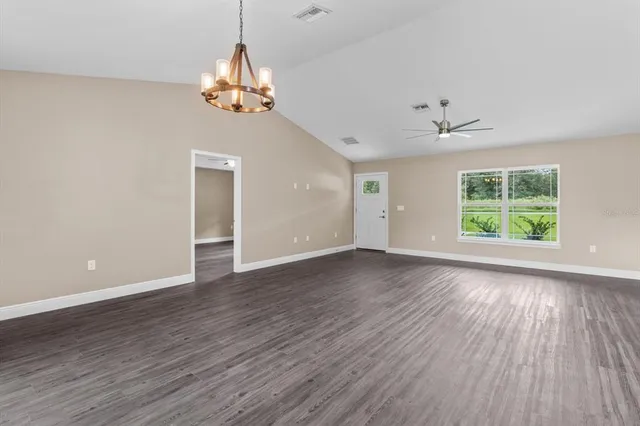 an empty room with wooden floor chandelier and windows