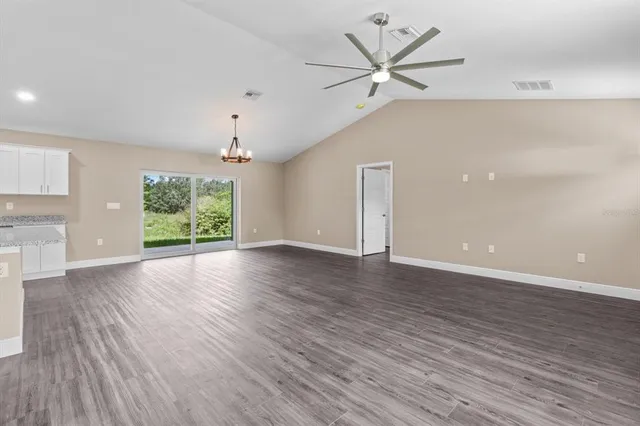 an empty room with wooden floor chandelier fan and windows