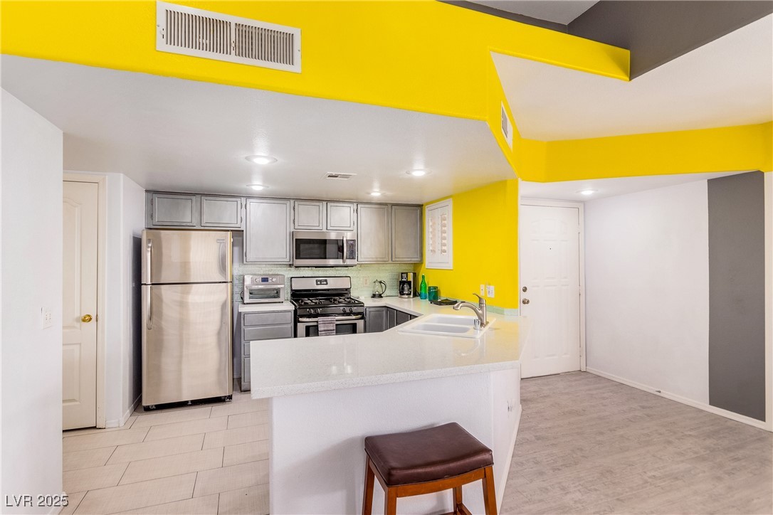 7400 West Flamingo Road, Unit 2006 Las Vegas, NV 89147 - Photo 7 of 30 Kitchen with appliances with stainless steel finishes, a peninsula, light countertops, a breakfast bar, and gray cabinets