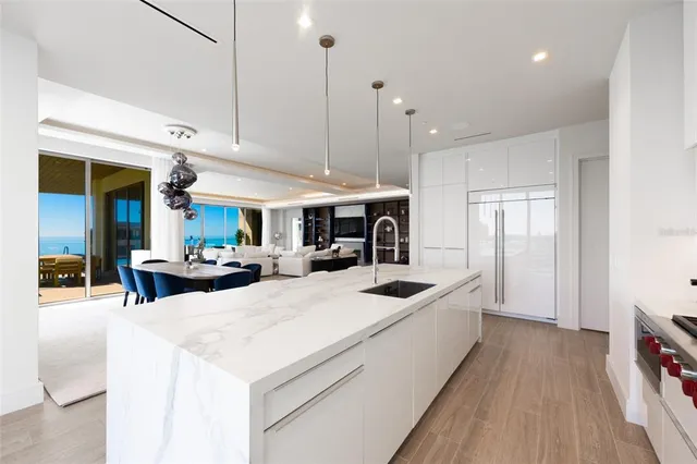 a open kitchen with stainless steel appliances kitchen island a stove a refrigerator a oven and a dining table with wooden floor