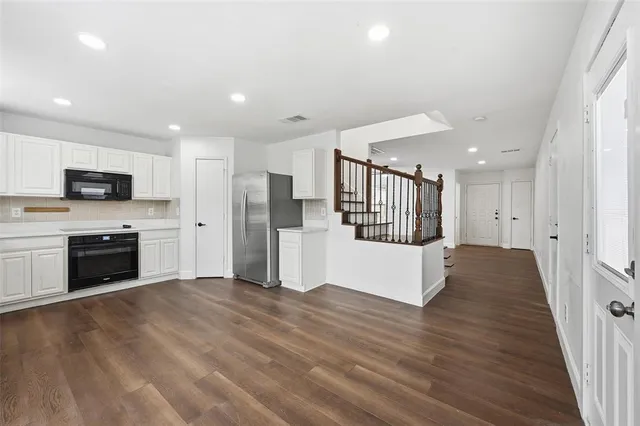 a large kitchen with a stove a sink dishwasher a refrigerator and white cabinets with wooden floor