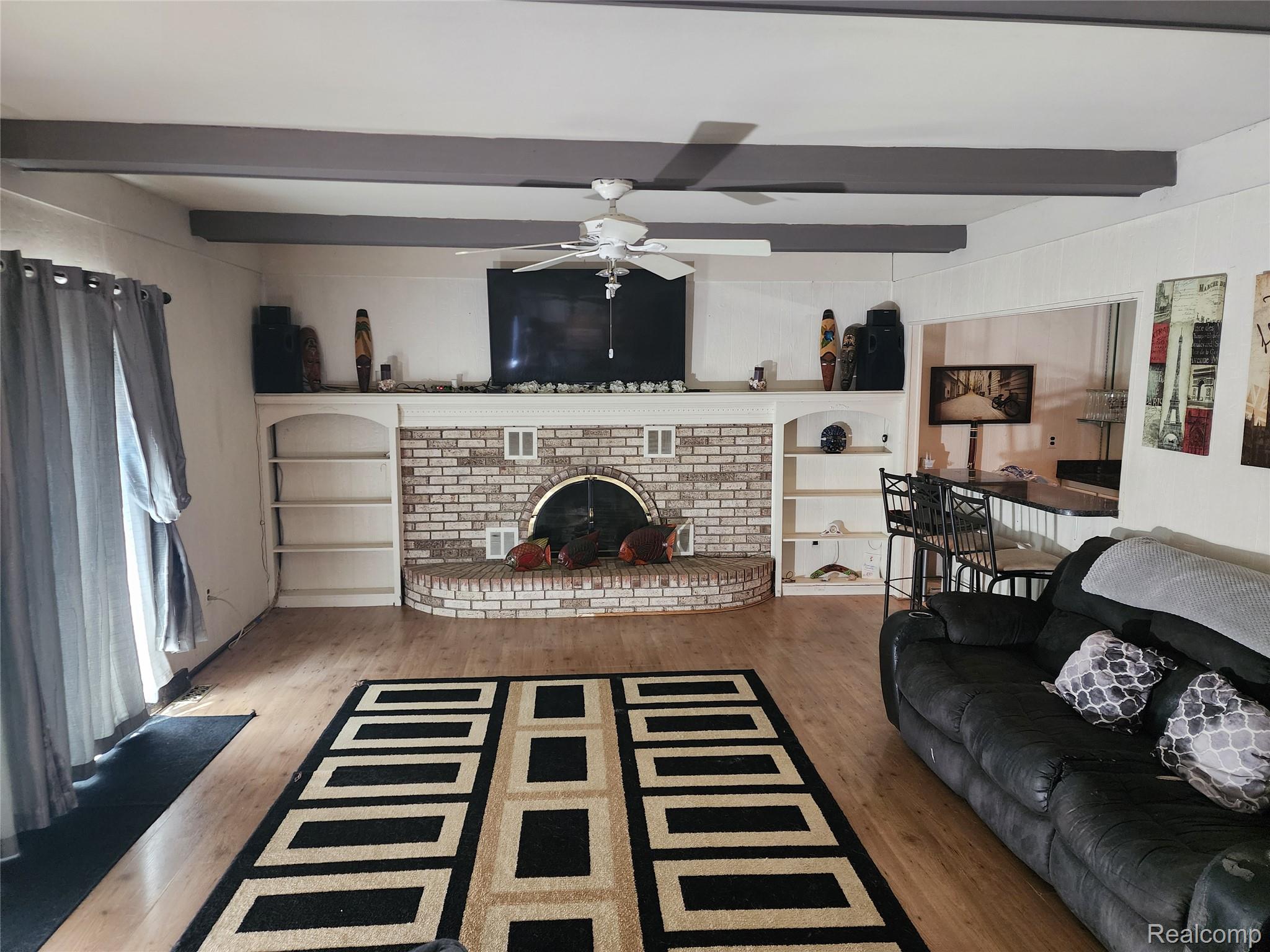 3333 Innsbrook Drive Rochester, MI 48309 - Photo 4 of 22 Open living space featuring wood-finish flooring, exposed ceiling beams, and a brick fireplace with a curved hearth