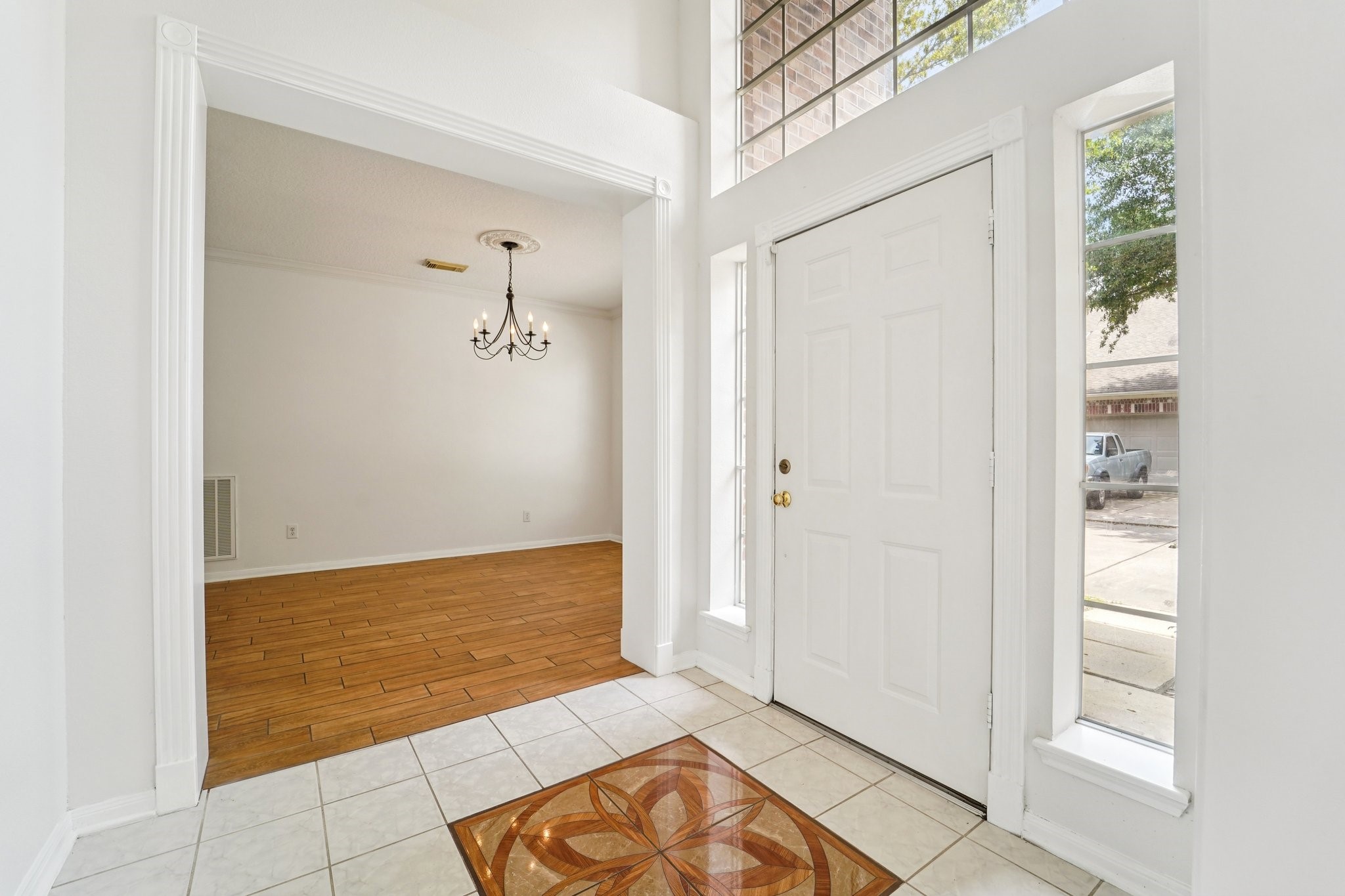 14420 Walters Road, Unit 55 Houston, TX 77014 - Photo 3 of 35 Bright entryway with a decorative tile inlay, high ceilings, and large windows. Adjacent is a room with wood flooring and a classic chandelier, offering a welcoming space for guests.
