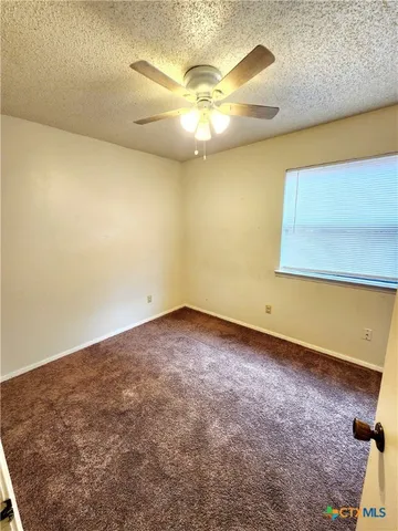 an empty room with a chandelier fan and wooden floor