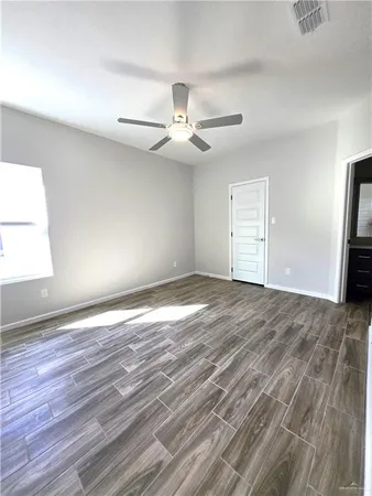 an empty room with wooden floor ceiling fan and windows