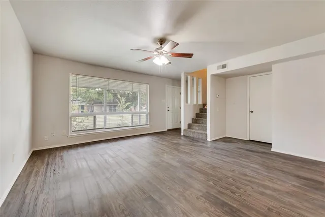 an empty room with wooden floor chandelier fan and windows