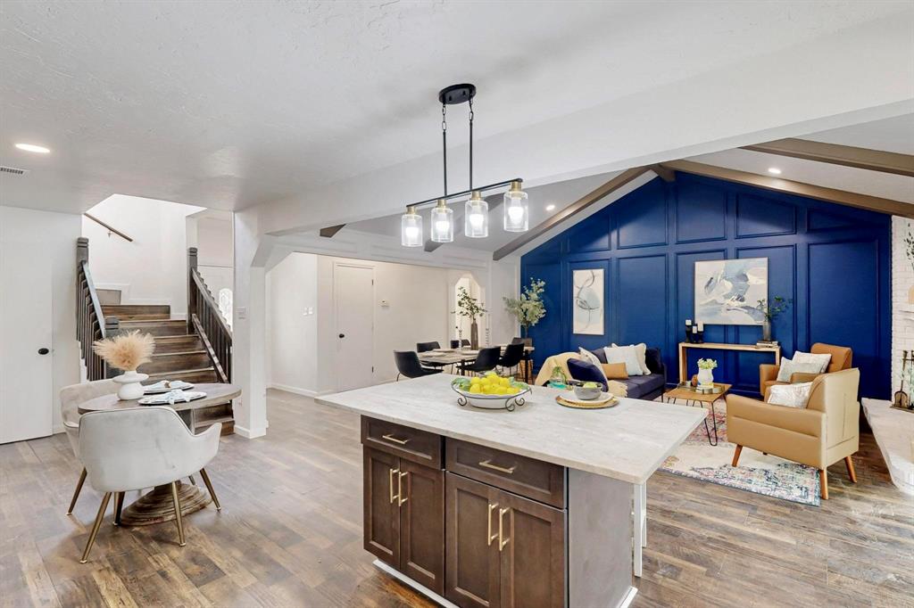 3965 Singleleaf Lane Fort Worth, TX 76133 - Photo 12 of 39 Open-concept living space with wood-finish flooring, a kitchen island featuring a light-toned countertop, a vaulted ceiling with exposed beams, and a striking blue accent wall with decorative paneling