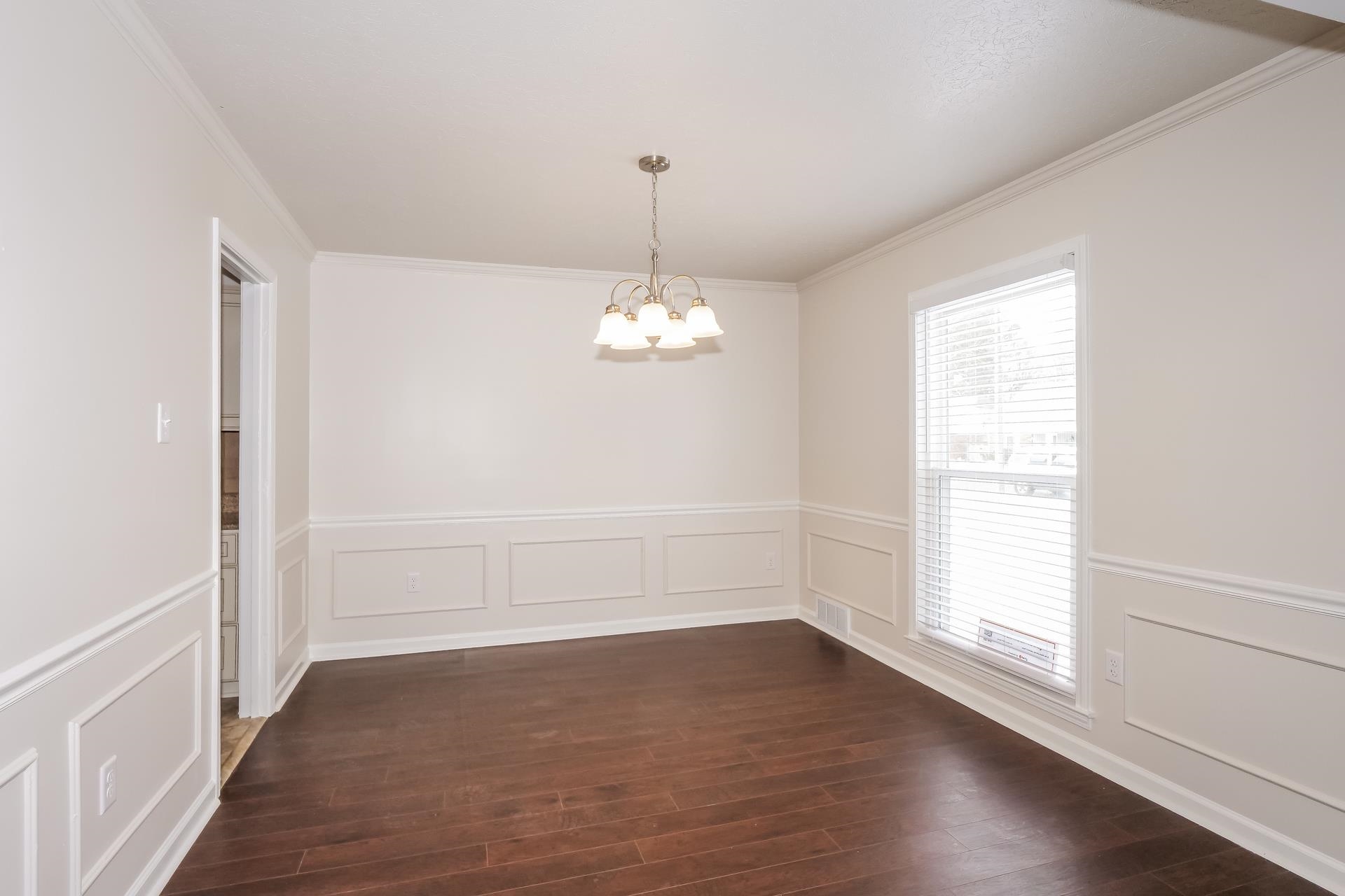 207 East Pecan Valley Street Collierville, TN 38017 - Photo 14 of 18 Unfurnished dining area featuring a decorative wall, a wainscoted wall, a chandelier, ornamental molding, and dark wood-style flooring