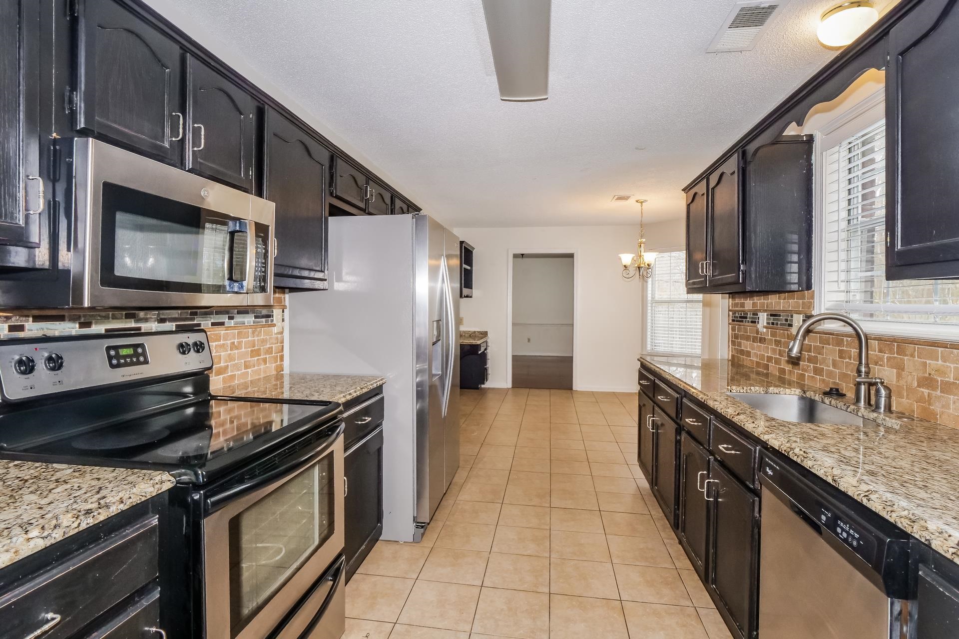 207 East Pecan Valley Street Collierville, TN 38017 - Photo 2 of 18 Kitchen with stainless steel appliances, light stone counters, decorative backsplash, light tile patterned floors, and a textured ceiling