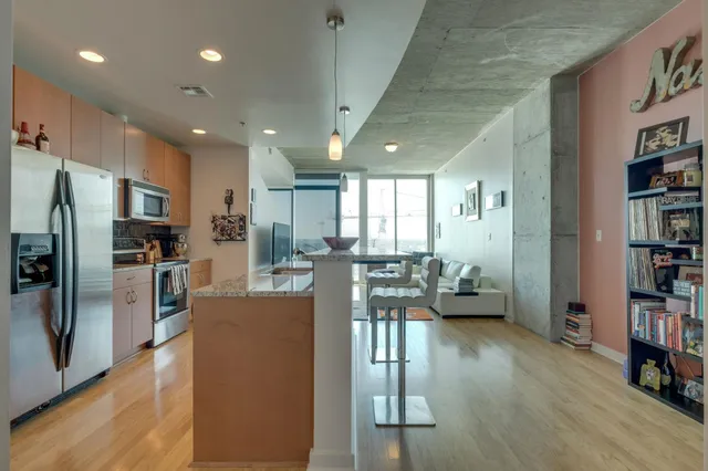 a kitchen with stainless steel appliances kitchen island granite countertop a refrigerator a stove a dining table and chairs with wooden floor