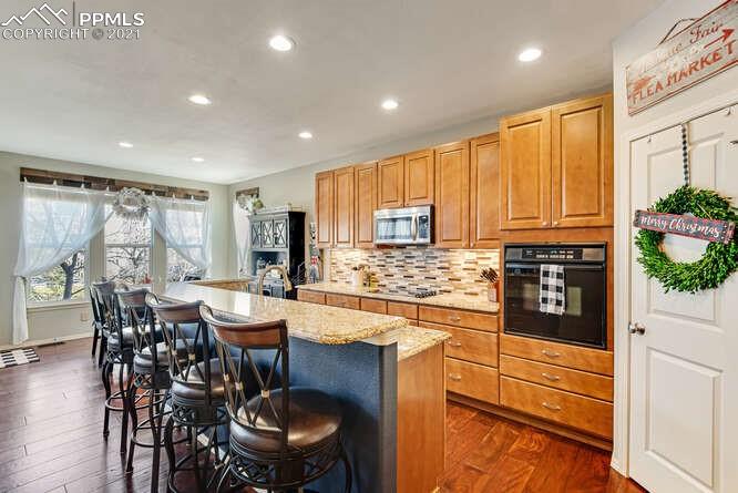 13873 Windy Oaks Road Colorado Springs, CO 80921 - Photo 12 of 28 a kitchen with stainless steel appliances granite countertop a stove a refrigerator a dining table and chairs with wooden floor