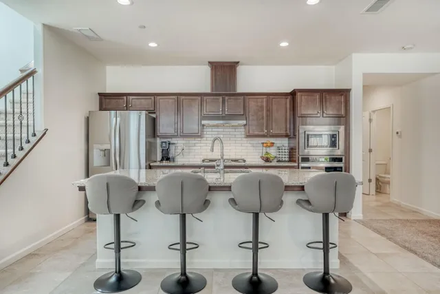 a kitchen with stainless steel appliances granite countertop a refrigerator a stove a sink counter space and chairs
