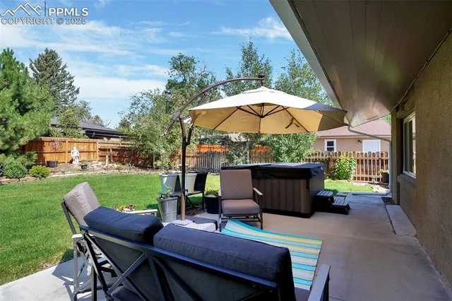 a view of patio with table and chairs under an umbrella with a garden