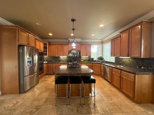 a kitchen with stainless steel appliances granite countertop a refrigerator a sink dishwasher a dining table and chairs with wooden floor