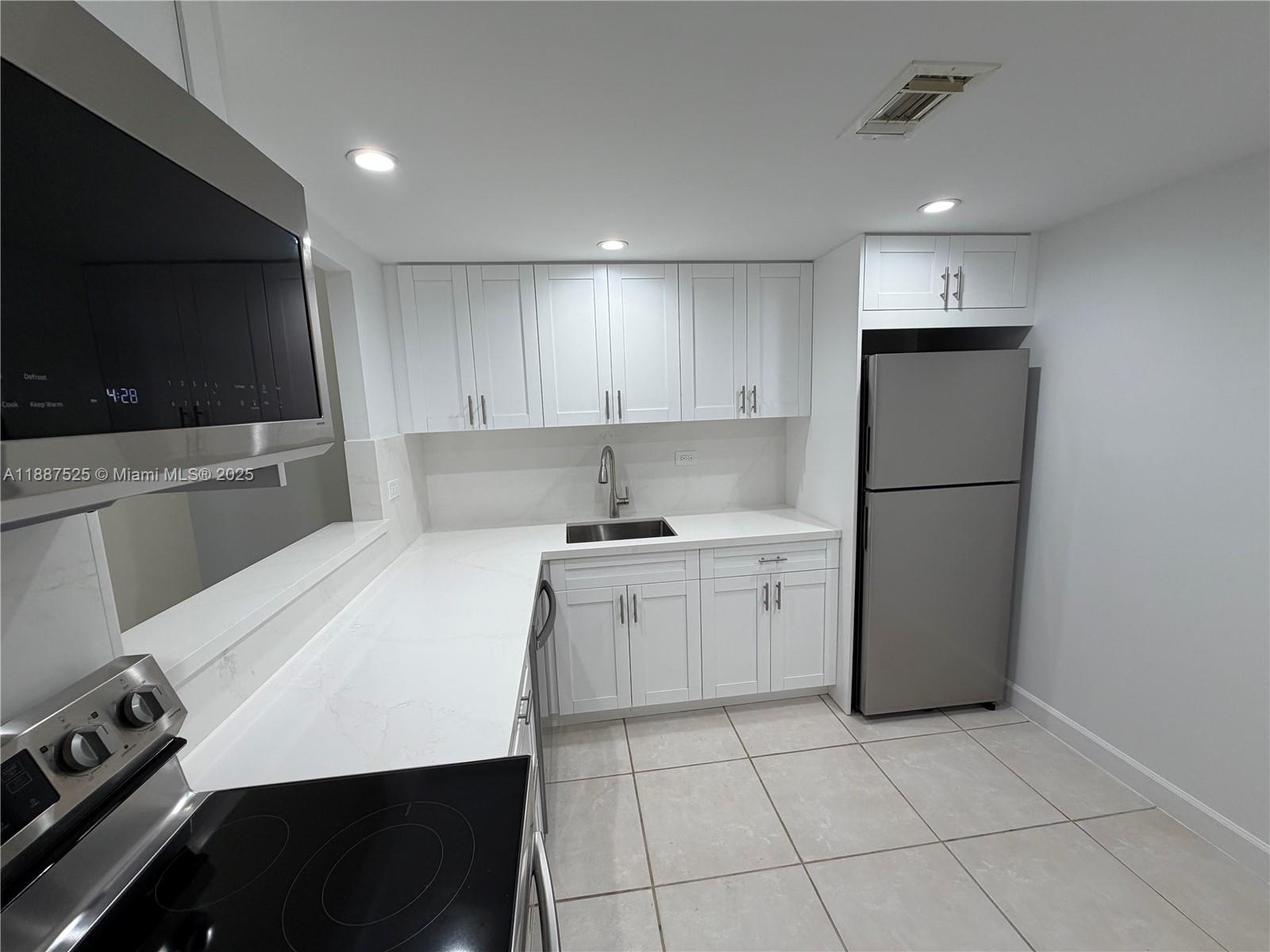 8101 Southwest 72nd Avenue, Unit 219W Miami, FL 33143 - Photo 16 of 30 a kitchen with a sink a refrigerator and a stove top oven with wooden floor