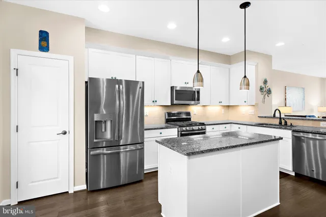 a kitchen with stainless steel appliances granite countertop a refrigerator a sink a stove and a wooden floors