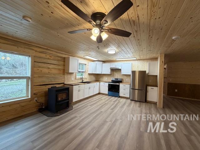 124 Windmill Lane Kooskia, ID 83539 - Photo 13 of 47 Kitchen with a wood stove, white cabinets, stainless steel appliances, wooden walls, and light wood finished floors