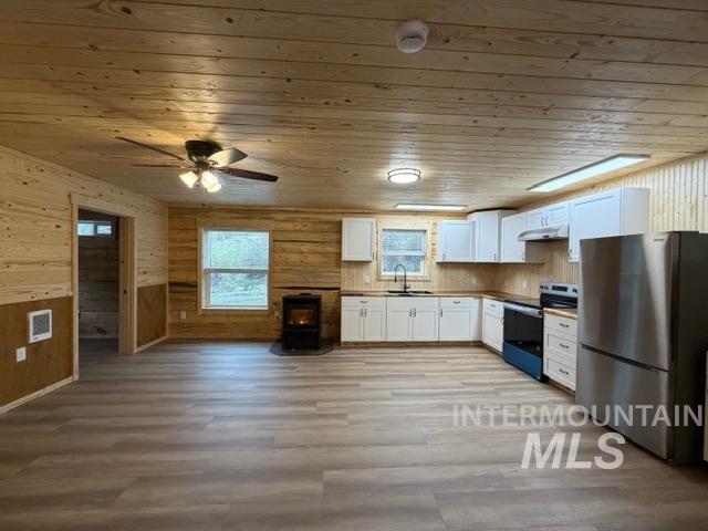 124 Windmill Lane Kooskia, ID 83539 - Photo 17 of 50 Kitchen featuring a wood stove, stainless steel appliances, white cabinetry, wood walls, and ceiling fan
