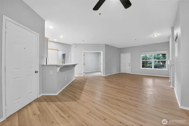 a view of an empty room and kitchen with wooden floor