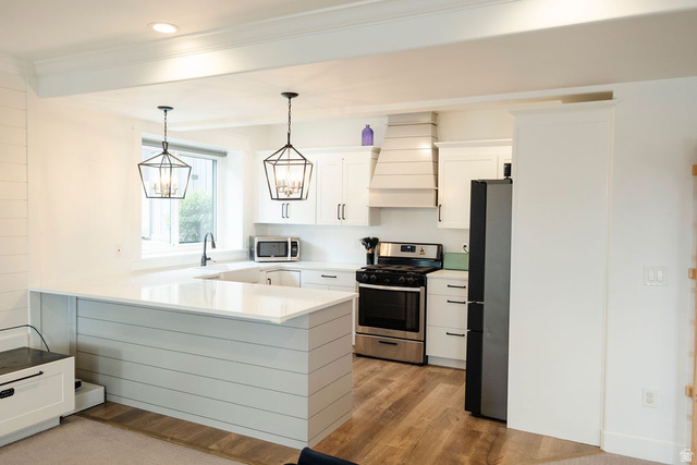 924 Country Lane Farmington, UT 84025 - Photo 51 of 91 Modern kitchen featuring white shaker cabinetry, stainless steel appliances, a custom range hood, wood-finish flooring, and two geometric pendant light fixtures