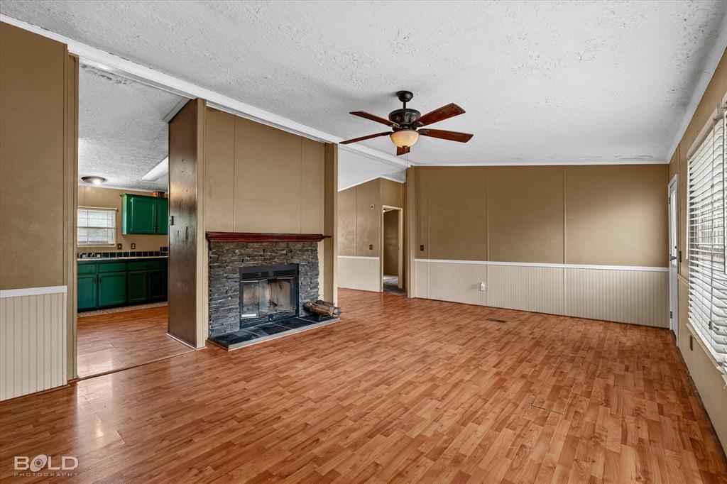 9720 Osburn Road Shreveport, LA 71129 - Photo 4 of 30 Living area featuring wood-finish flooring, a stone-clad fireplace, and an integrated ceiling fan